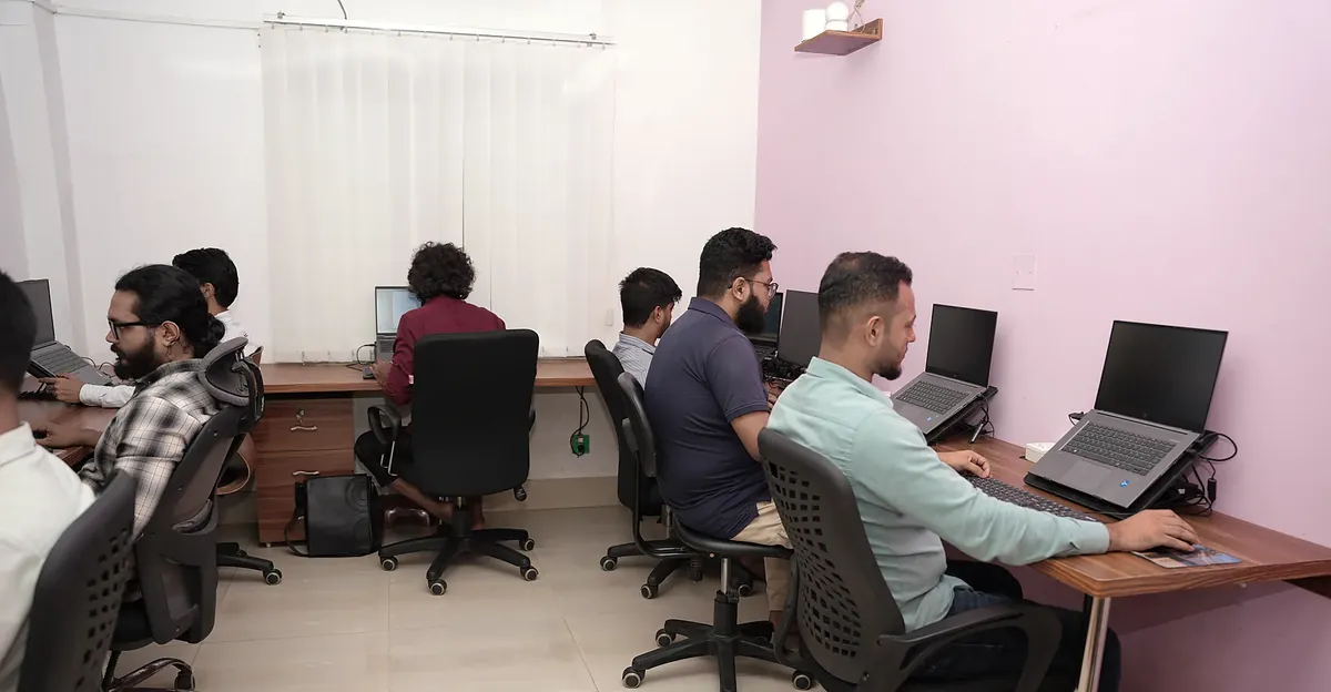 A row of people working at laptops along a lilac wall